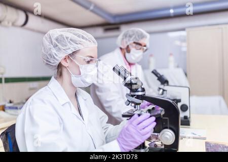 uomo e donna scienziati che guardano attraverso il microscopio in laboratorio Foto Stock
