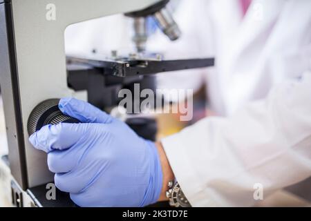 vista laterale ravvicinata della mano di uno scienziato anonimo che regola un microscopio in laboratorio Foto Stock
