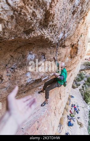 arrampicatore che offre la mano ad un altro collega mentre appende su una corda Foto Stock