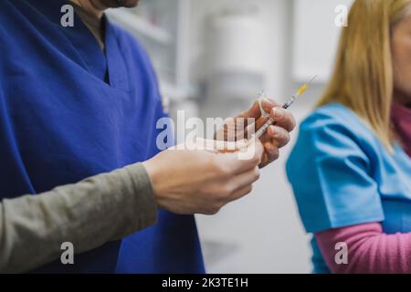 Vista laterale di medici di raccolto in siringa di tenuta uniforme con vaccino in stanza medica su sfondo sfocato Foto Stock