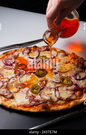 La ragazza versa una gustosa pizza con salsicce bavaresi e jalapeno con olio di pepe caldo Foto Stock