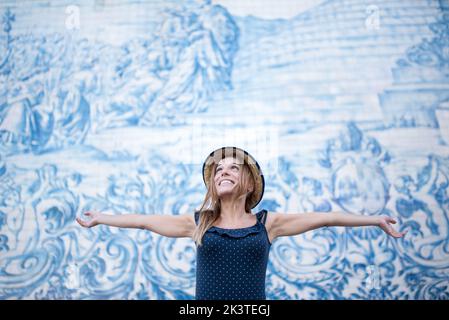 Giovane viaggiatore felice in cappello di paglia che guarda contro il muro con affresco durante il viaggio a Porto Portogallo Foto Stock