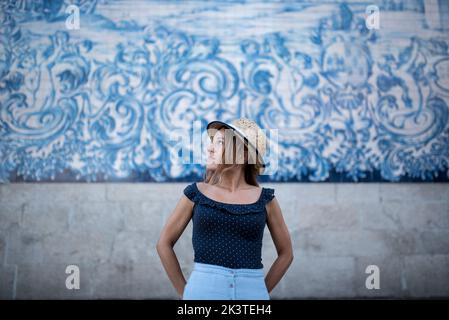 Giovane viaggiatore felice in cappello di paglia guardando via contro il muro con affresco durante il viaggio a Porto Portogallo Foto Stock