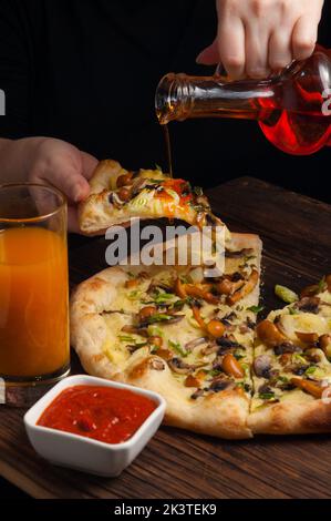 la ragazza versa burro speziato sulla gustosa pizza con funghi. concetto: vegetarianismo Foto Stock