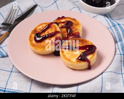 gustose torte di formaggio casolare versate con marmellata di frutti di bosco su un piatto rosa in un bar Foto Stock