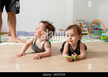 Adorabile bambino ragazzo e ragazza in abiti simili giacendo sul pavimento mentre si gioca a casa con raccolto irriconoscibile padre Foto Stock
