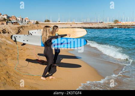 Vista laterale di giovani e felici surfisti in mute in piedi con tavole da surf sulla spiaggia di sabbia nei giorni estivi Foto Stock