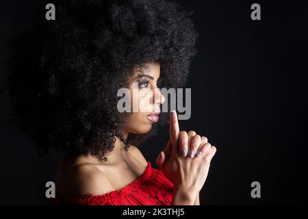 Vista laterale di una giovane donna cubana con acconciatura afro che mostra un gesto di pistola mentre guarda avanti Foto Stock