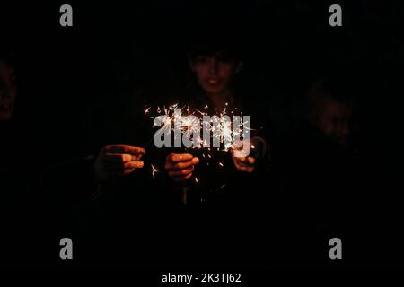 Gruppo di giovani amici irriconoscibili e sfocati che giocano con scintille sulla foresta Foto Stock