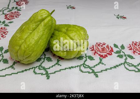 Due chayotes freschi su una tovaglia con fiori rossi a punto croce, noti anche come: Labu siam, jipang, verdure biologiche. Concetto di bio, biol Foto Stock