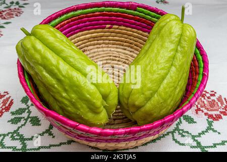 Due chayotes in cestino messicano di vimini su tovaglia a punto incrociato, noto anche come: Labu siam, jipang, verdure coltivate in modo biologico. Concetto di bio, biol Foto Stock