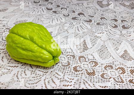 Vista frontale del chayote con il suo gambo su tavola con tovaglia a maglia marrone fine, noto anche come: Labu siam, jipang, verdure biologiche. Concetto Foto Stock