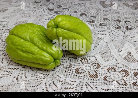 Due chayote verdi con i loro gambi su tavola con tovaglia a maglia marrone fine, noto anche come: Labu siam, jipang, verdure coltivate in modo biologico. Concetto Foto Stock