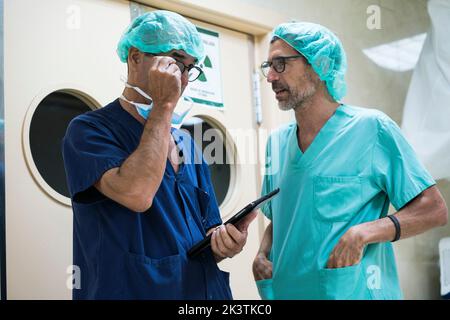 Due uomini in chirurgo uniforme in piedi nel corridoio dell'ospedale e utilizzando un tablet moderno insieme Foto Stock