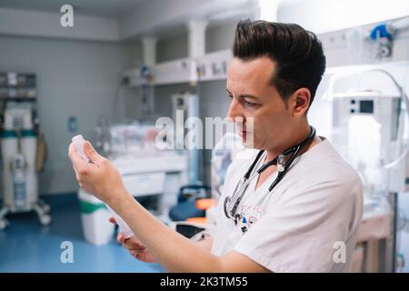 Pediatra in siringa bianca a riempimento uniforme con vaccino per iniezione in camera con incubatori per neonati in ospedale Foto Stock