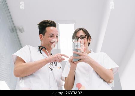 Coppia di pediatri in uniforme bianca con telefono che cammina lungo il corridoio della clinica dopo la fine del turno di lavoro Foto Stock