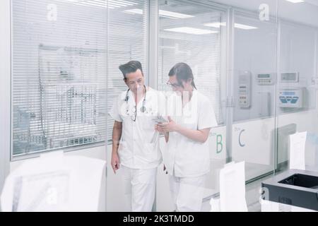 Coppia di pediatri in uniforme bianca con telefono che cammina lungo il corridoio della clinica dopo la fine del turno di lavoro Foto Stock