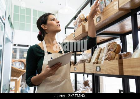 Basso angolo colpo di imprenditrice di panetteria latino-americana femmina che guarda la sua merce Foto Stock