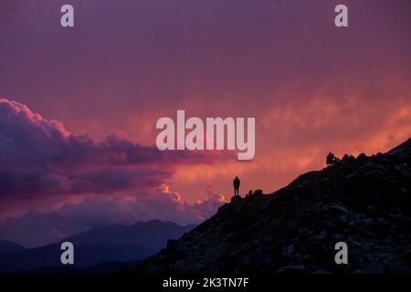 Silhouette di esploratore anonimo distante in piedi da solo sul pendio di collina contro cielo nuvoloso tramonto in montagne dei Pirenei Foto Stock