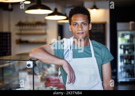 Giovane operaio del negozio di alimentari latino-americano che si appoggia al bancone Foto Stock