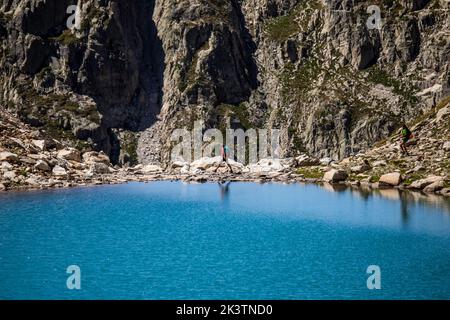 Avventuriero lontano e irriconoscibile con zaino che cammina da solo sulla costa rocciosa tra il lago blu e la roccia ripida nei Pirenei Foto Stock