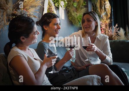 Ritratto di gruppo di tre amici femminili felici e diversi che si appendono e che si bevono vino nella wine bar alla moda Foto Stock