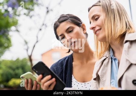 Vista laterale ad angolo basso di due imprenditrici che si scambiano informazioni sui loro smartphone mentre lavorano all'aperto Foto Stock