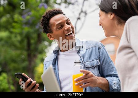 Immagine laterale con angolazione ridotta di una coppia eterogenea che ride mentre condivide contenuti dai social media Foto Stock