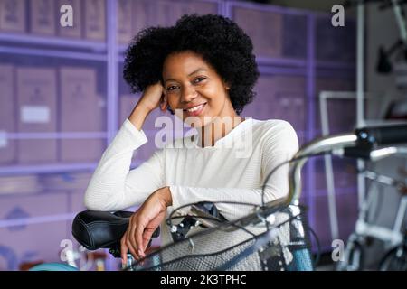 Ritratto a metà strada di una donna afro-americana in piedi nel suo negozio di biciclette Foto Stock