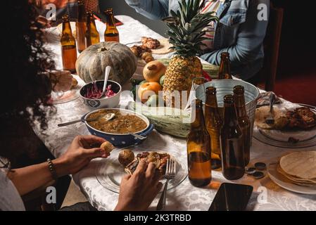 Raccogli un gruppo anonimo di amici che mangia un pasto gustoso mentre si adunano al tavolo con frutta e birra e piatti fatti in casa e che si divertiscono durante il fine settimana insieme Foto Stock
