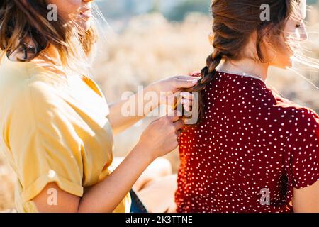 Vista posteriore di giovani amici donne irriconoscibili seduti su un terreno roccioso sui capelli intrecciati della collina Foto Stock