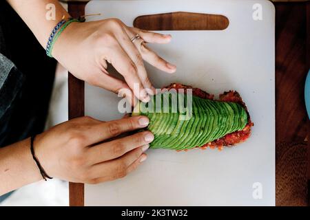 Da sopra cuocete preparare il panino e impilare l'avocado affettato sul pane su un supporto bianco Foto Stock