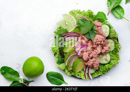 Insalata di tonno con avocado, cetriolo, cipolla rossa e lattuga. Sfondo in pietra bianca, vista dall'alto, spazio copia Foto Stock