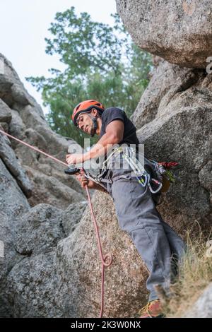 Da sotto arrampicatore in elmetto reggendo la corda e compagno di assicurazione che striscia sulla montagna a strapiombo Foto Stock