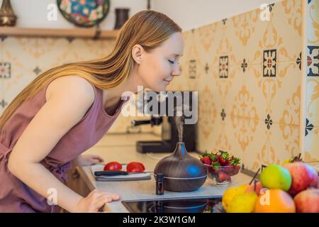 La donna prepara il cibo accanto a un diffusore di aroma. La cuoca taglia i peperoni rossi maturi in cucina. Cucina insalata di peperoni freschi, maturi per gli ospiti. Estate Foto Stock