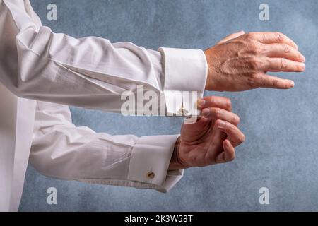 Un uomo bottoni la sua camicia bianca con gemelli d'oro Foto Stock