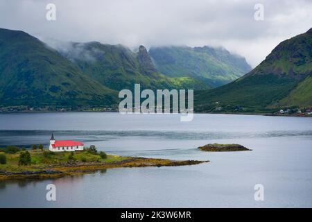 Vista di Austnesfjorden con la chiesa di Sildpollnes contro le montagne nuvolose, Lofoten, Norvegia Foto Stock