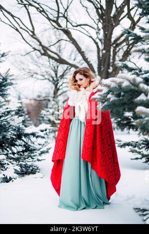 Una bella ragazza in abiti da fiaba rossa cammina attraverso una foresta innevata Foto Stock