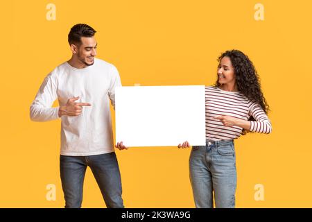 Controllare. Sorridente arabo uomo e donna che indica bianco Placard Foto Stock