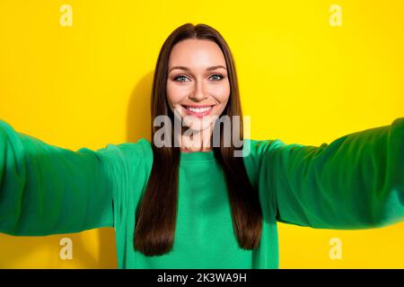 Foto selfie sorridente carino giovane donna attraente bella beaming blogger che mostra nuovo pullover verde isolato su sfondo giallo Foto Stock