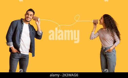 Coppia araba romantica che comunica attraverso Tin Phone su sfondo giallo Foto Stock