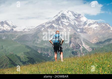 Donna Backpacker con uno zaino in piedi e godere di piste innevate di montagna Kazbek 5054m mentre lei cammina da verde erba collina. Moun del Caucaso orientale Foto Stock