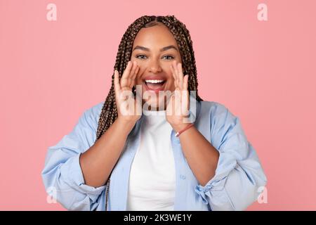 Donna africana eccitata urla tenendo le mani vicino al viso, sfondo rosa Foto Stock