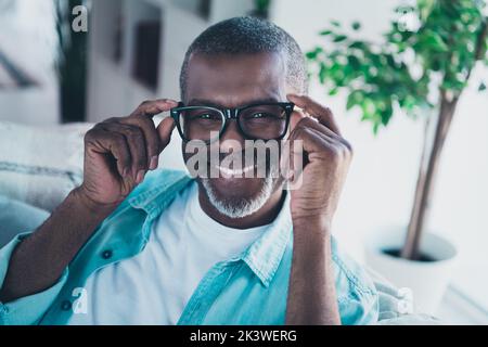 Ritratto di uomo anziano positivo sedersi in casa moderna soggiorno prova godere di nuove specifiche ottiche offerta speciale Foto Stock