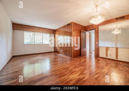 Stanza vuota con una parete coperta da un murale in legno verniciato di un colore che si abbina ai pavimenti in parquet, un'altra con specchi e un lampadario di cristallo o Foto Stock