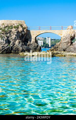 Palma, Maiorca, Spagna. Es Pujolar sulla spiaggia di Cala Major, un piccolo ponte verso una piccola isola vicino alla costa. Sullo sfondo la città di CAS Catala o S. Foto Stock