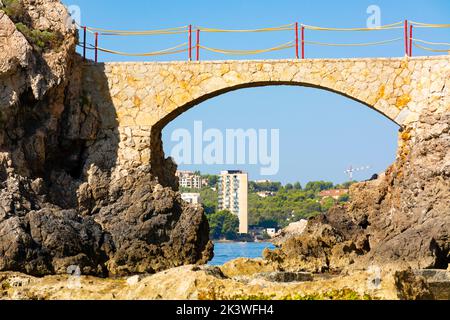 Palma, Maiorca, Spagna. Es Pujolar sulla spiaggia di Cala Major, un piccolo ponte verso una piccola isola vicino alla costa. Sullo sfondo la città di CAS Catala o S. Foto Stock