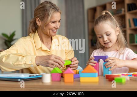 Preparazione alla scuola. Felice bambina preschooler giocare sviluppando giochi di legno con psicologo professionista Foto Stock