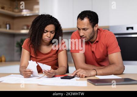 Triste uomo nero e donna disperata, con tablet, pagare fatture e tasse insieme in cucina Foto Stock