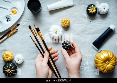 Dipingere con le mani femminili zucche nere e dorate. Idee creative di pittura della zucca per Halloween e il Ringraziamento per gli adulti. Semplice zucca facile Foto Stock